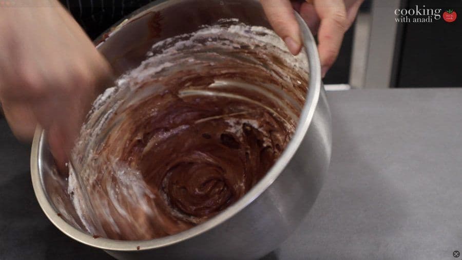 Chocolate mousse batter being folded together in a white bowl with a spatula