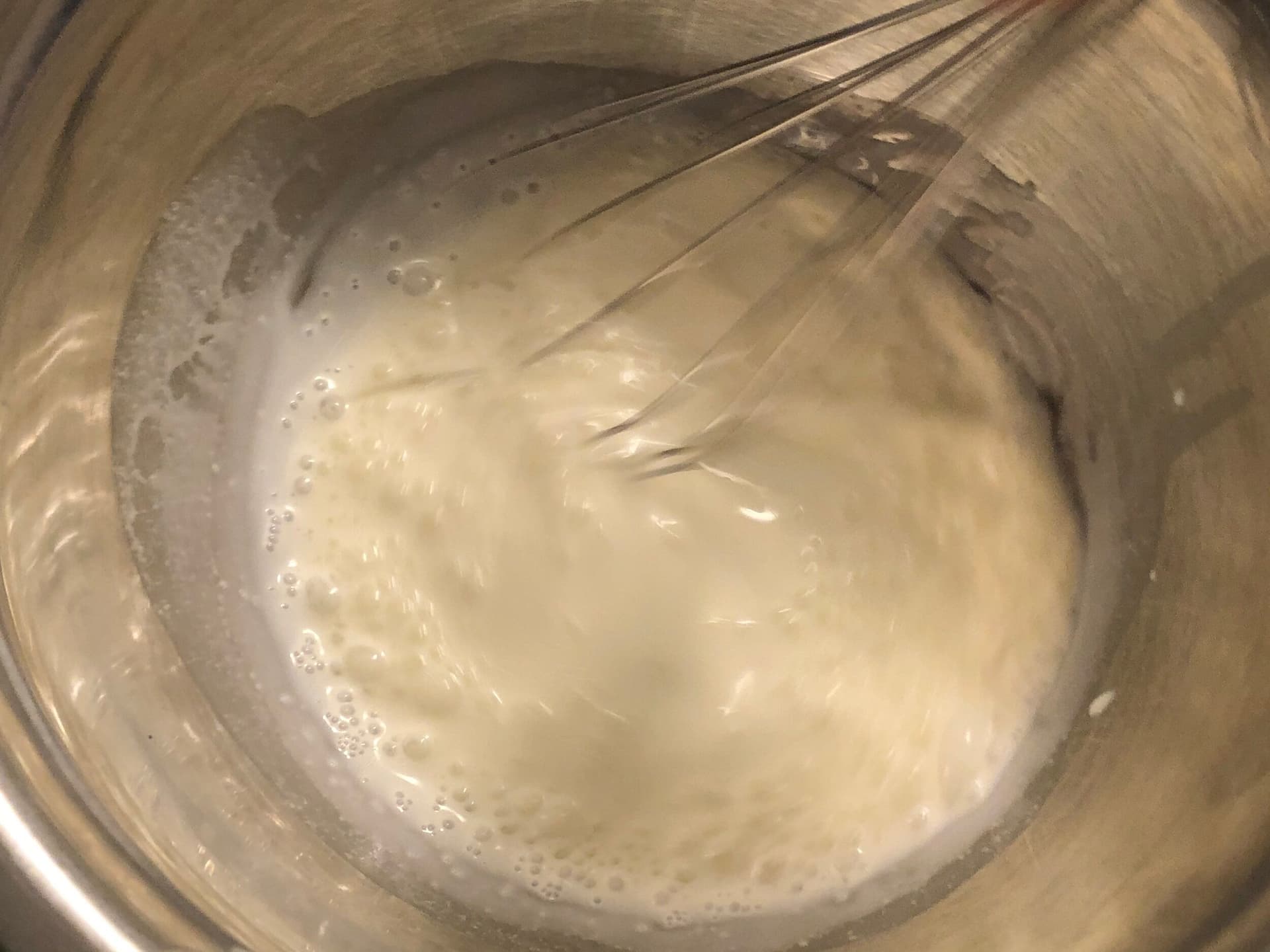 Partially whipped cream in a bowl being whisked, showing thickened but still liquid consistency.