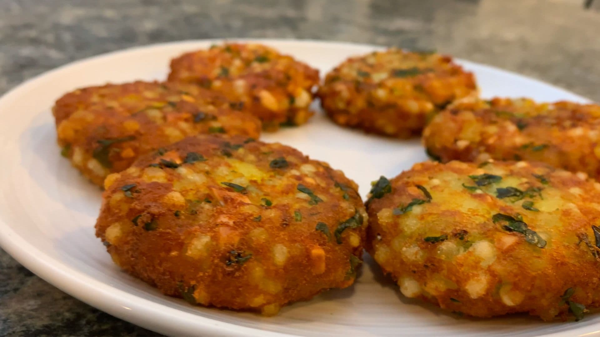 Golden-brown sabudana aloo tikkis garnished with fresh herbs on a white plate, ready to serve.