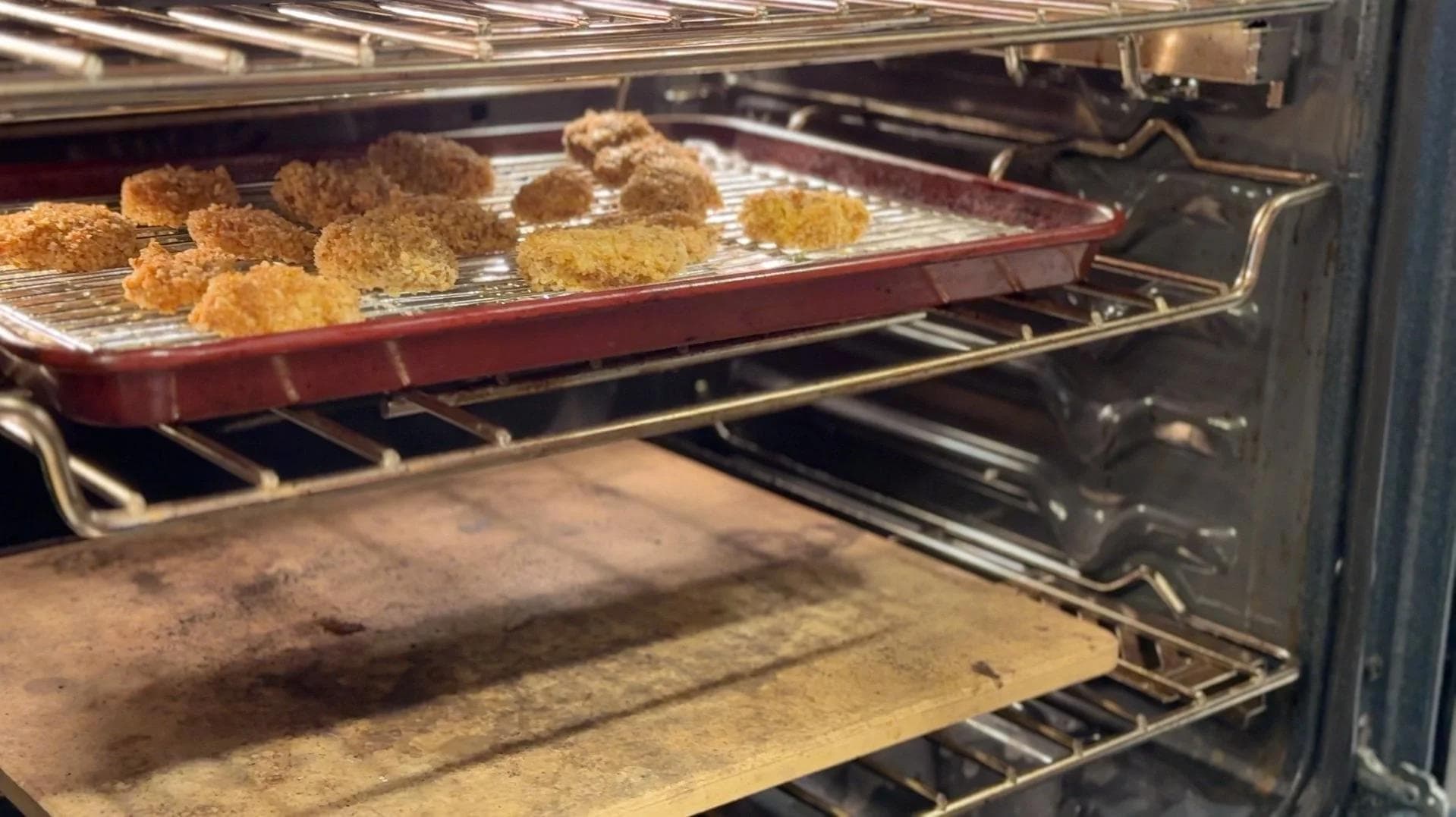 Golden panko chicken nuggets baking on a wire rack lined baking tray in the oven.
