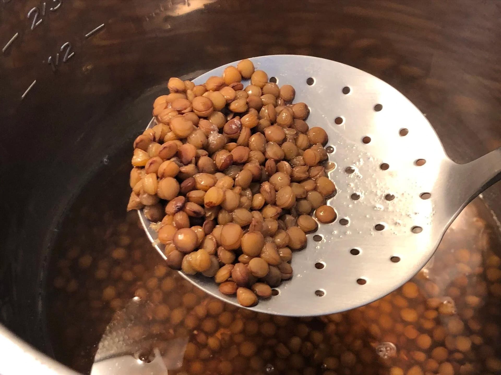Cooked lentils being strained in a white colander over a pot of cooking liquid.