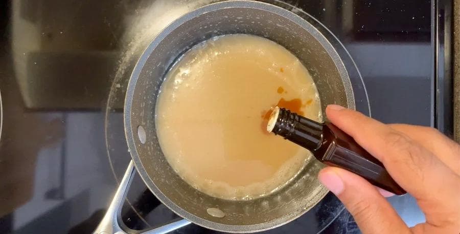 Vanilla extract being drizzled into a pan of rich caramel sauce while whisking