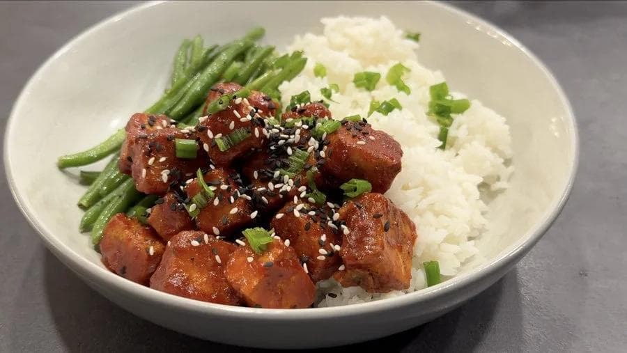 Crispy Korean-style tofu bites glazed with sauce and sesame seeds, served with steamed rice, green beans, and green onions.