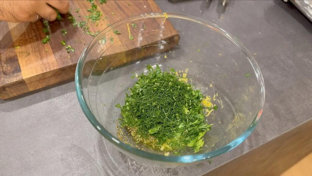 Herb marinade with chopped fresh dill and parsley mixed with olive oil and lemon in a glass bowl.