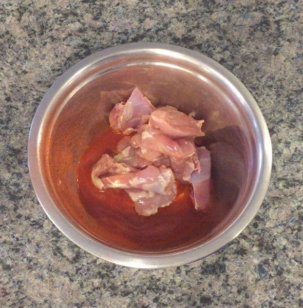 Raw chicken pieces marinating in red liquid with lemon juice, Kashmiri mirch, and salt in a stainless steel bowl.