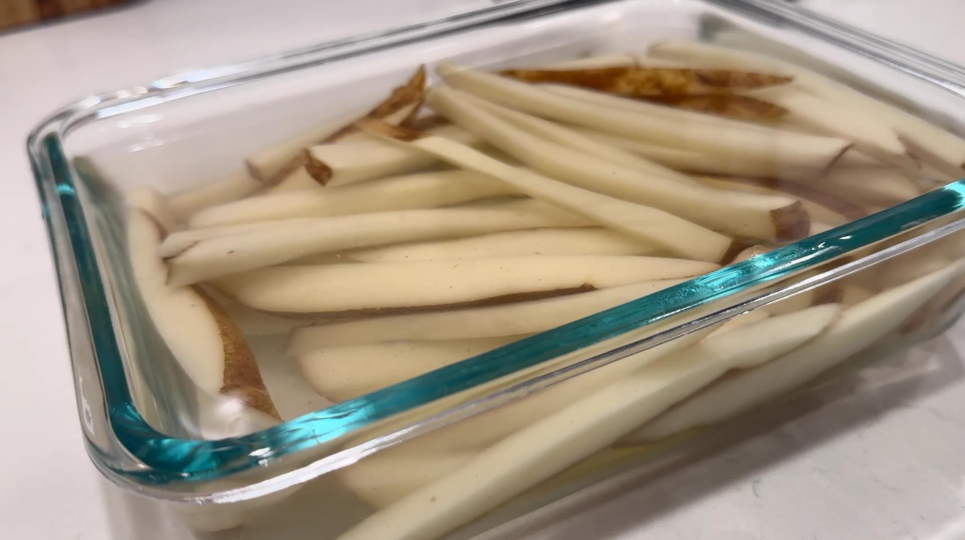 Peeled potato strips soaking in cold water in a glass baking dish.