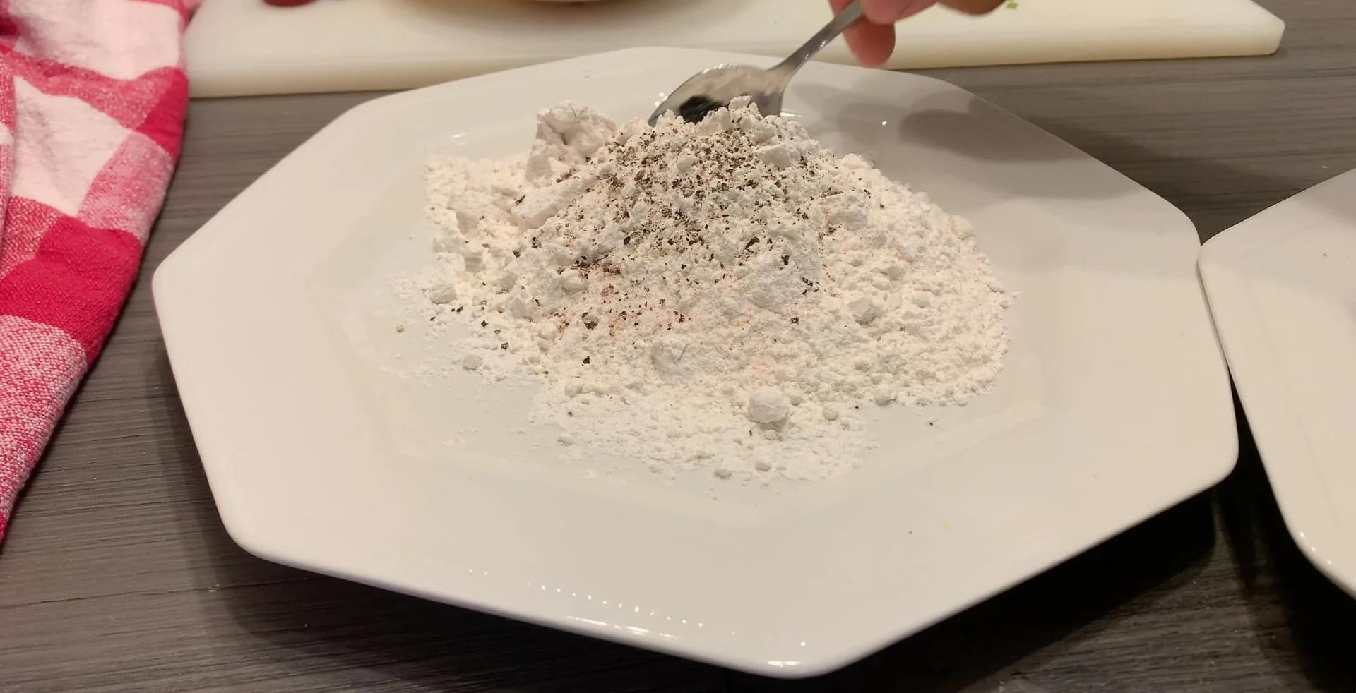 Seasoned all-purpose flour mixed with salt and pepper on a white plate with a spoon.