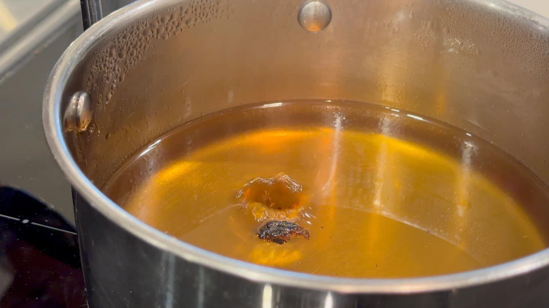 Sugar and water mixture dissolving in a saucepan on the stove with golden syrup consistency.