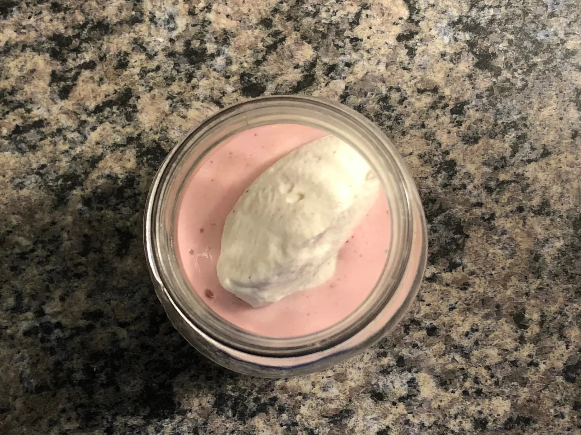 Strawberry cheesecake smoothie in a glass jar topped with a dollop of whipped cream on a granite countertop.