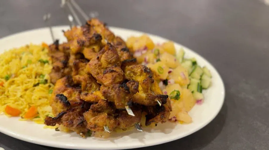 Grilled chicken satay skewers with yellow rice and diced potato salad on a white plate.