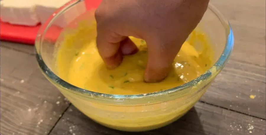 Hand mixing paneer pieces into yellow besan batter in a glass bowl.