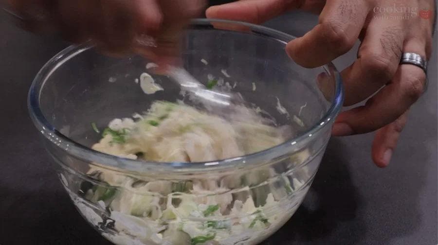 Crab salad mixture with mayo, green onions, and seasonings being mixed in a glass bowl.