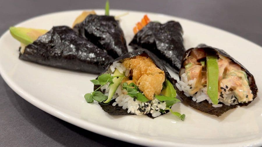 Five black nori sushi cones filled with rice, vegetables, and protein on a white plate.
