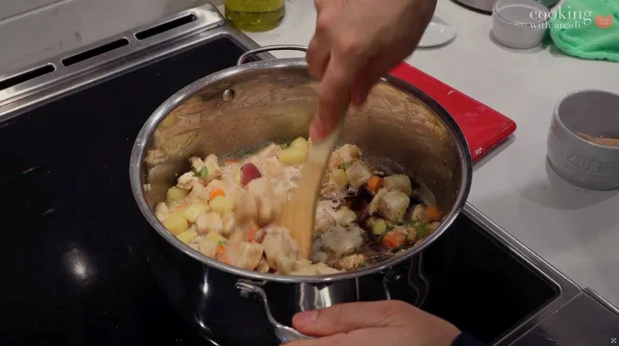 Stirring chicken and vegetable filling in a pot with a wooden spoon during preparation of Guinness chicken pot pie.