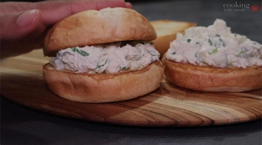 Toasted buns filled with creamy crab salad garnished with fresh herbs, served on a wooden board.