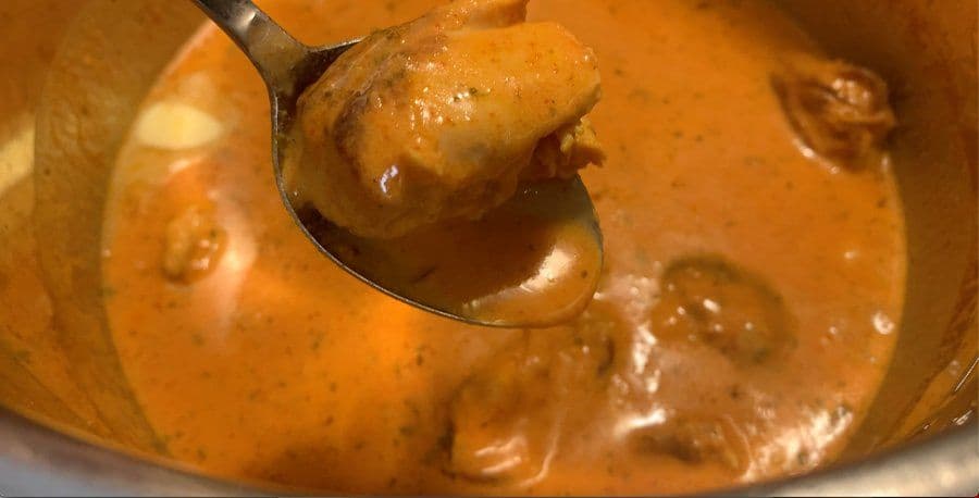 Spoon lifting creamy orange butter chicken sauce from pot, demonstrating thick, coat-the-spoon consistency.