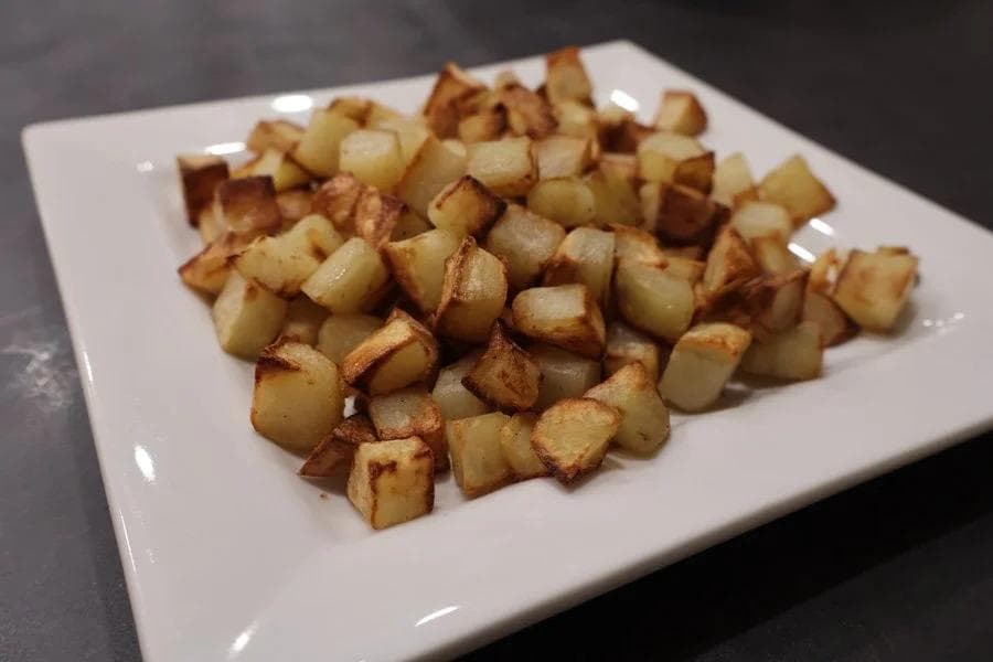 Crispy golden cubed roasted potatoes served on a white plate with browned, caramelized edges