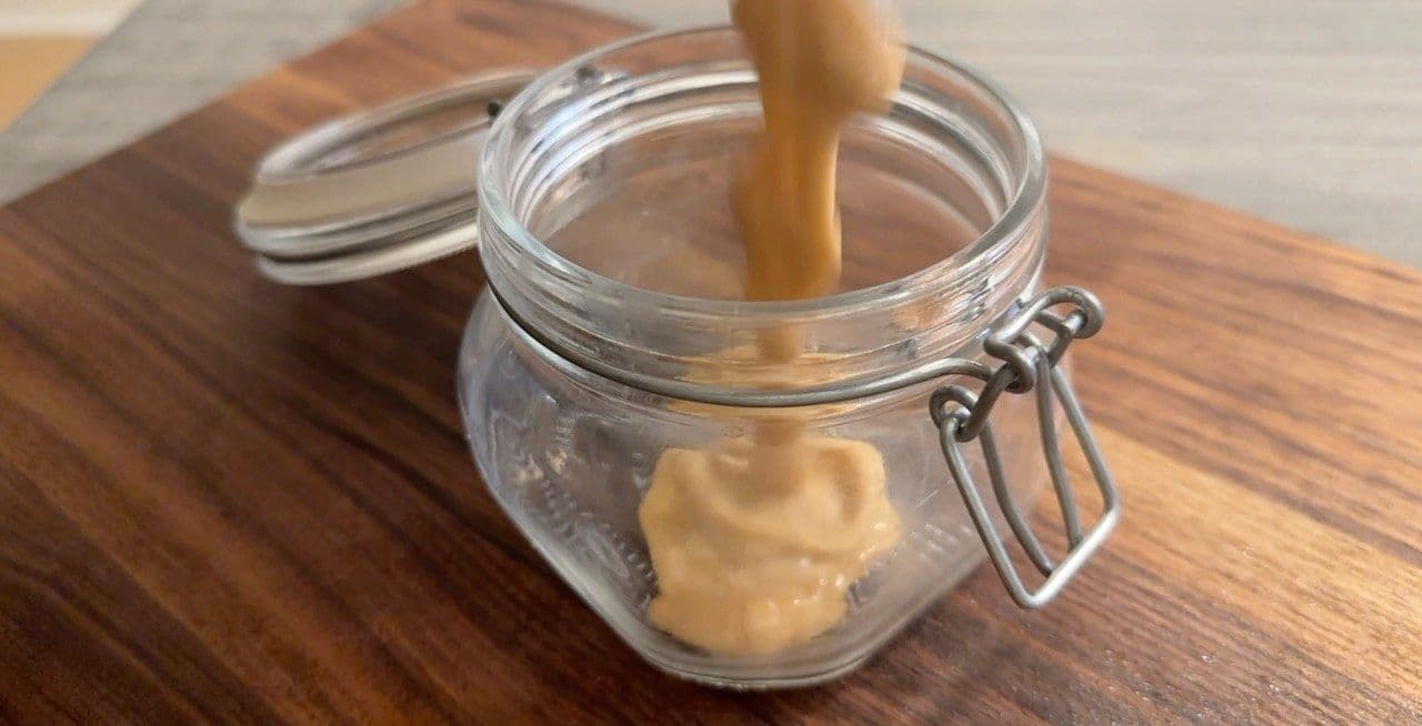 Homemade lactose-free condensed milk being poured into a glass jar on a wooden surface.