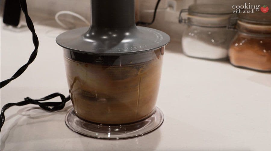 Spice paste blended with oil in food processor bowl, showing tan-colored mixture.