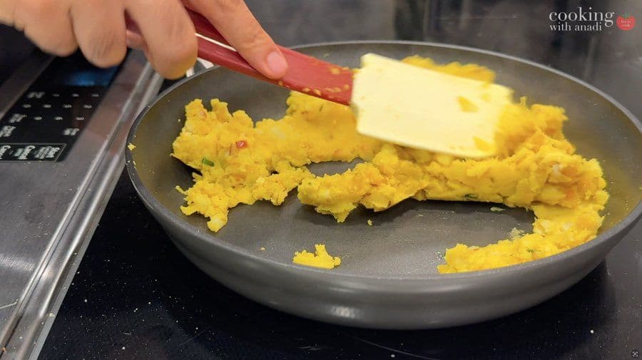 Stirring cooked golden yellow spiced potatoes in a gray pan with a red spatula.