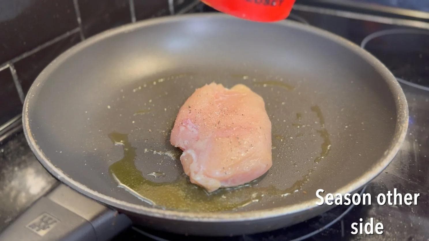 Chicken breast seared in garlic oil in a pan, ready to flip and cook the other side.