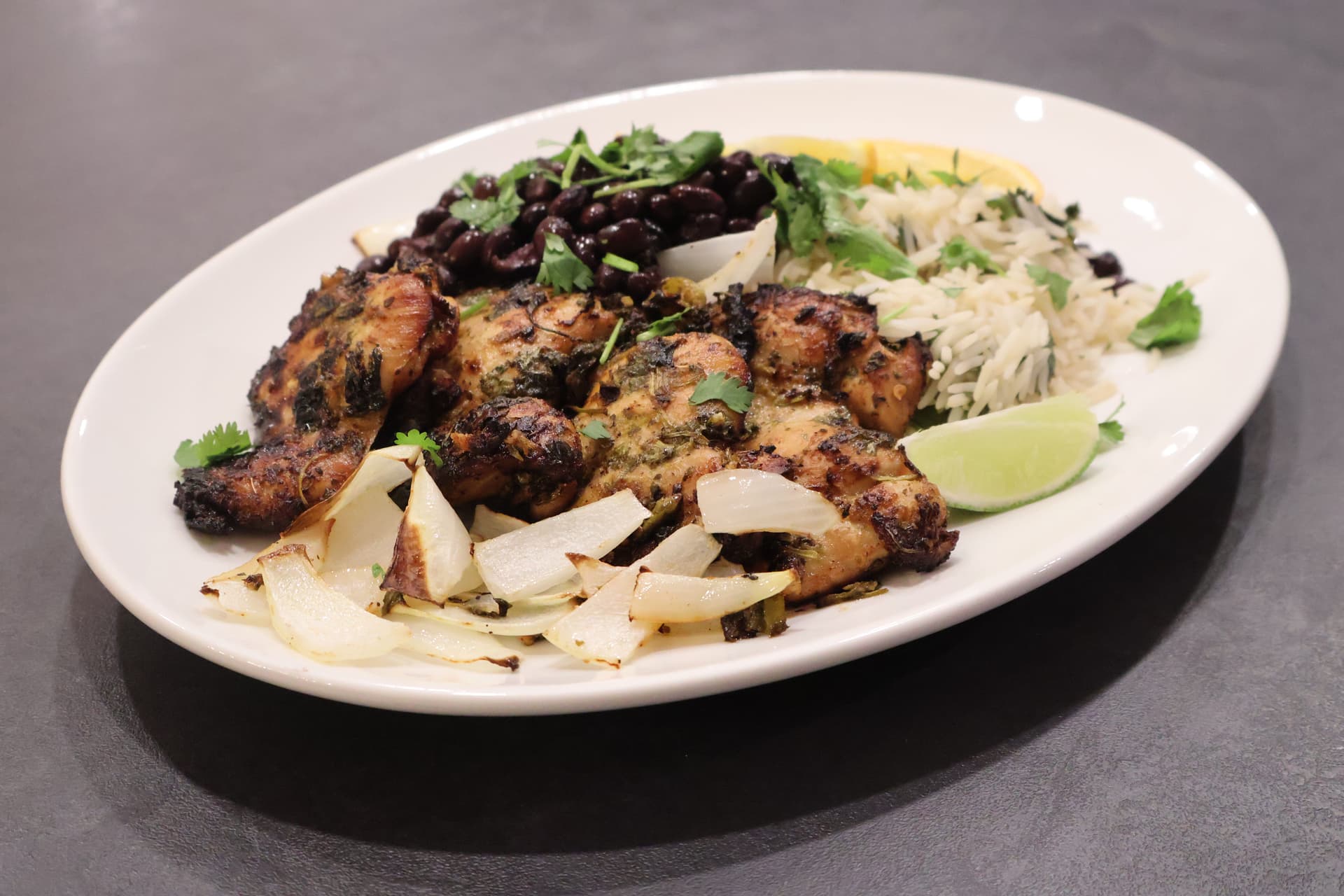 Cuban mojo chicken served on white plate with shredded cabbage, black beans, lime wedge, and cilantro garnish.