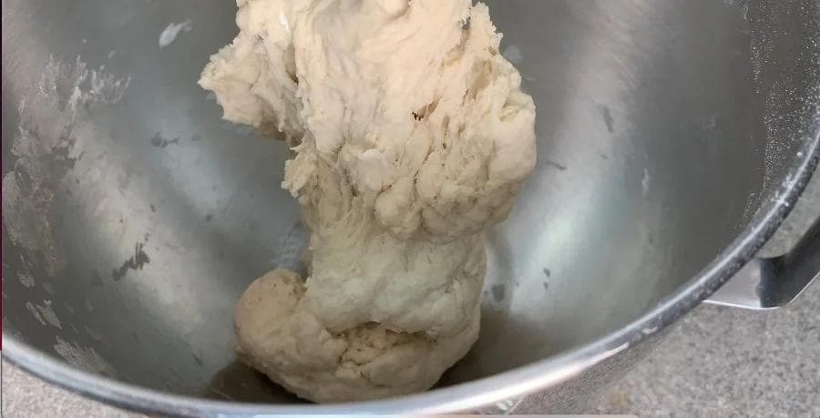 Soft pizza dough kneaded in a metal mixing bowl with a dough hook attached to a stand mixer.