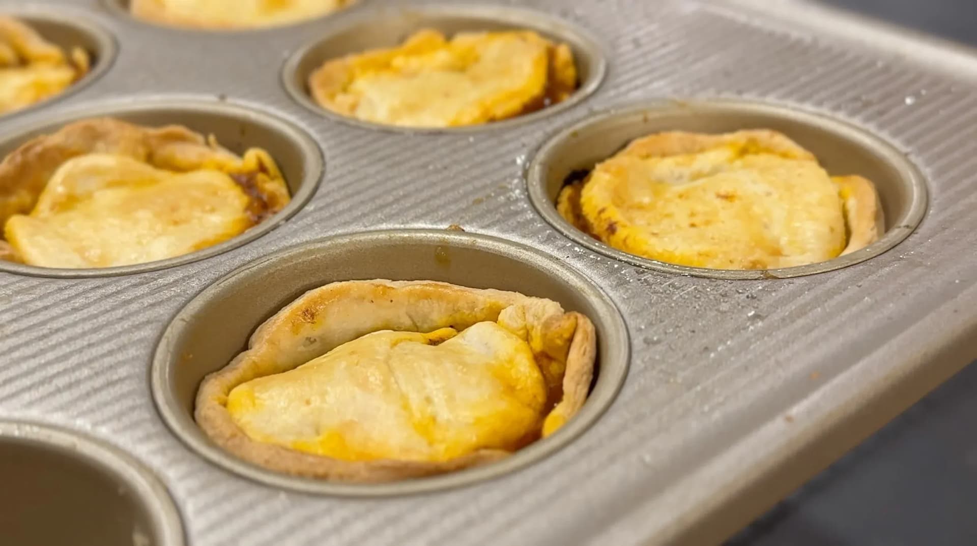 Baked Belizean meat pies in a muffin tin, golden brown with flaky pastry crusts.