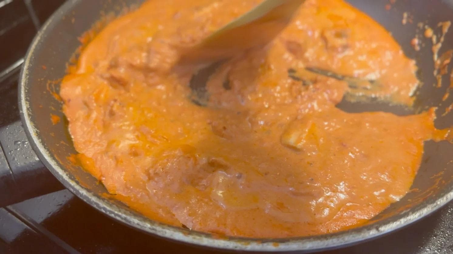 Creamy tomato sauce with diced chicken and pasta mixed together in a pan, ready for parmesan cheese.