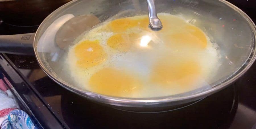 Eggs cooking in a covered pan with butter, yolks intact and whites setting on medium heat.