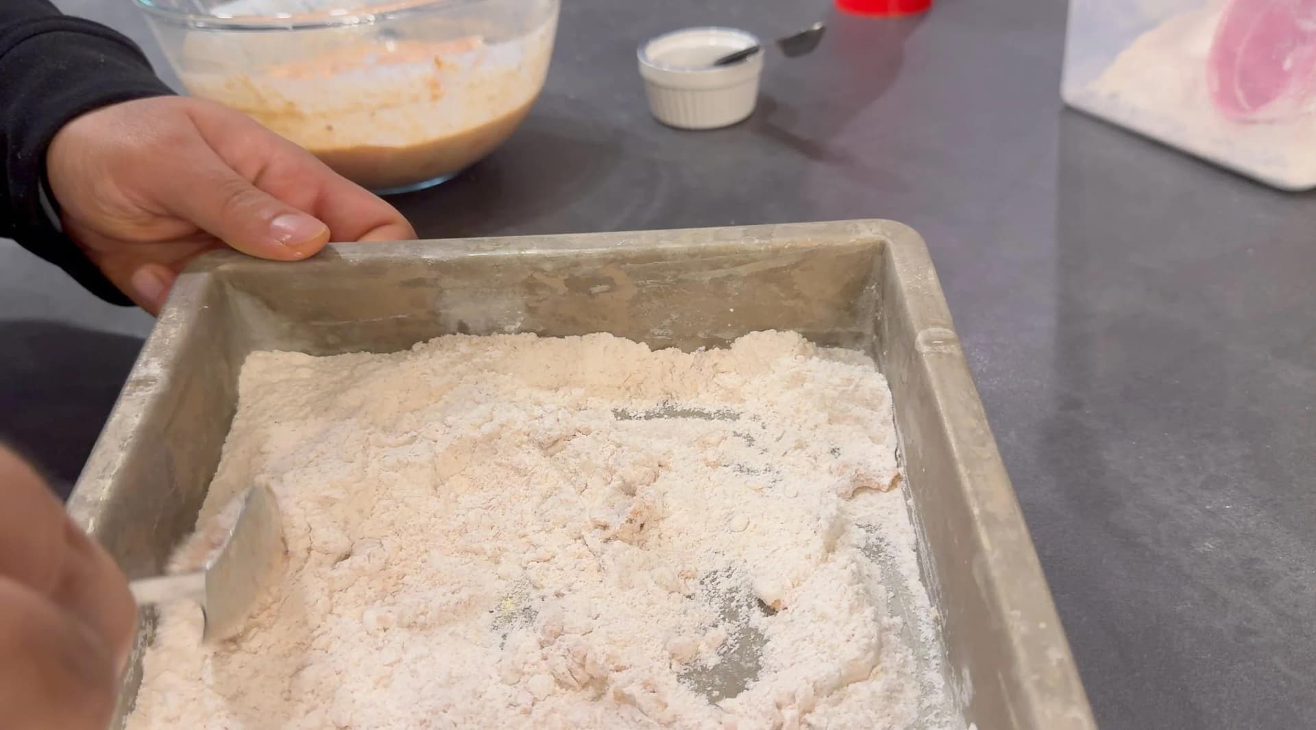 Flour mixture with salt, pepper and baking powder in a rectangular baking dish, partially mixed with buttermilk marinade.