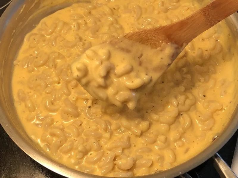 Creamy cheese sauce with cooked macaroni being stirred with a wooden spoon in a pot.