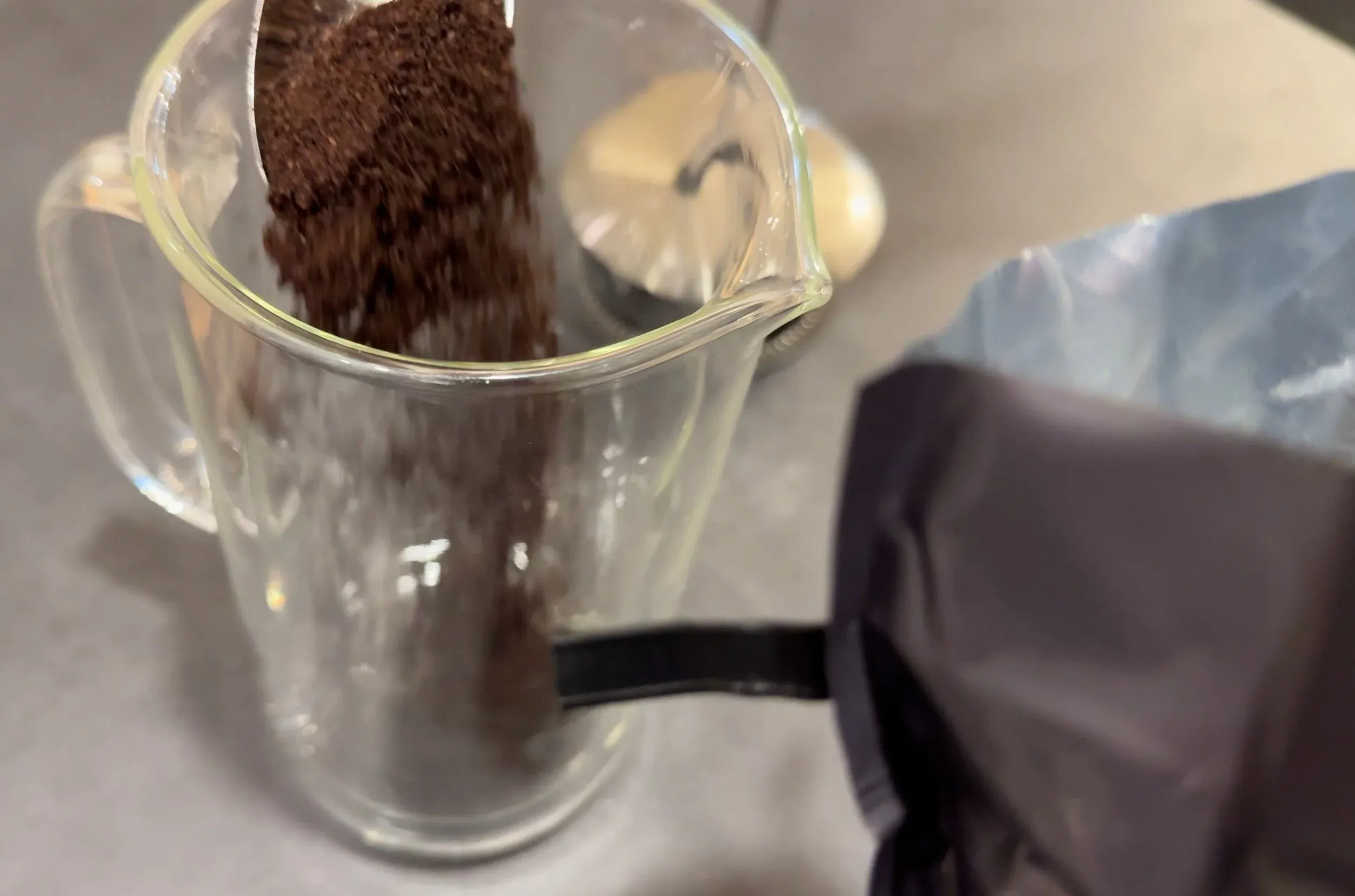 Ground coffee being poured into a glass measuring cup for an iced pumpkin spice latte.