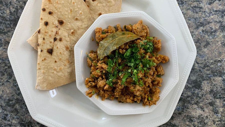 Chicken keema served on a white plate with roti and bay leaf garnish, topped with fresh cilantro.