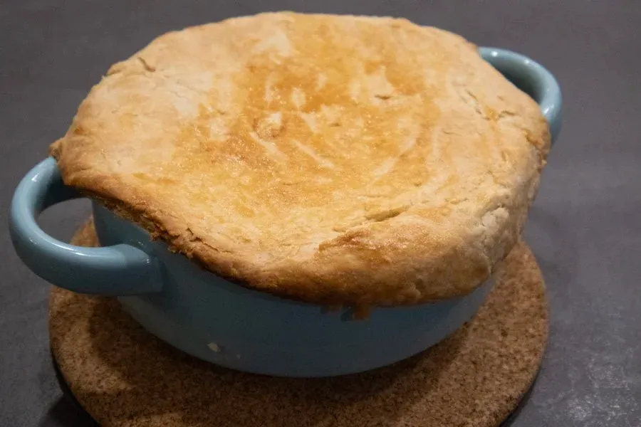 Baked chicken pot pie in a blue ceramic dish with handles, sitting on a cork trivet.