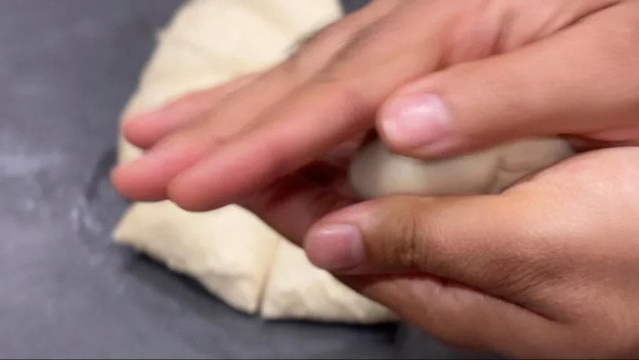 Hands shaping and flattening a ball of Lebanese pita dough on a dark surface.