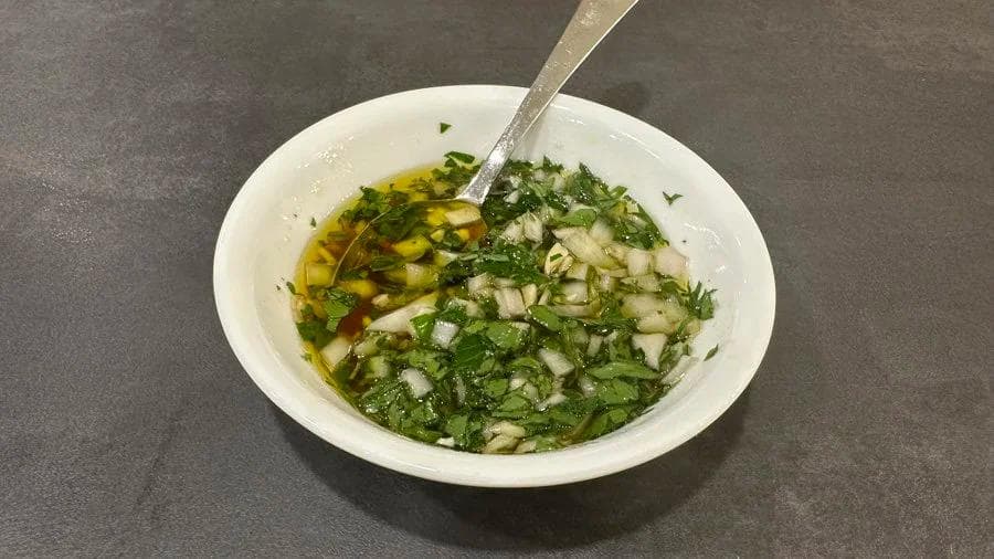 Chimichurri verde sauce in a white bowl with fresh parsley, garlic, and olive oil being stirred together.