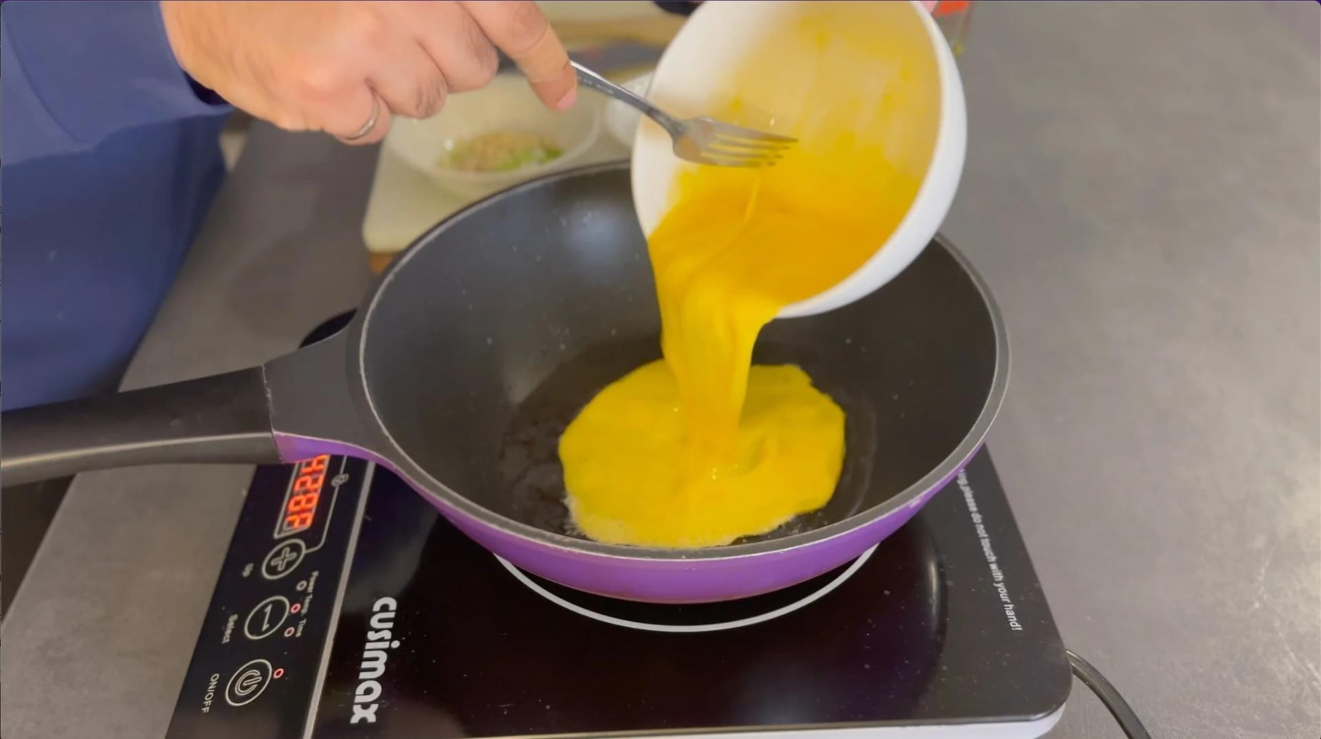 Whisked eggs being poured into a hot purple wok with oil, beginning to scramble.