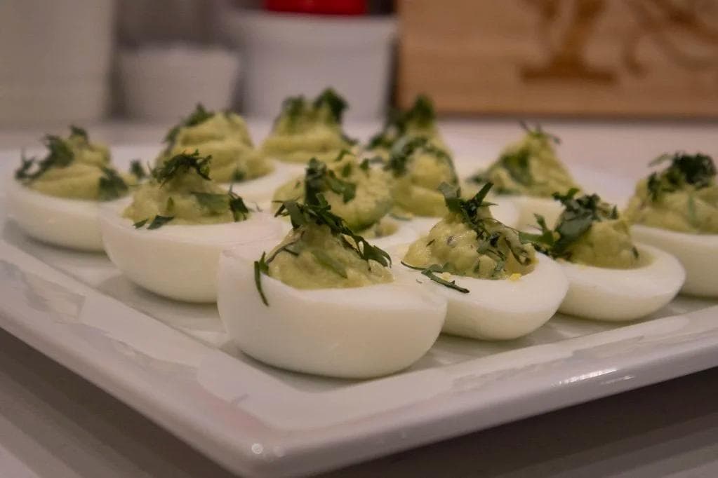 St. Patrick's Day avocado deviled eggs garnished with fresh parsley on a white plate.