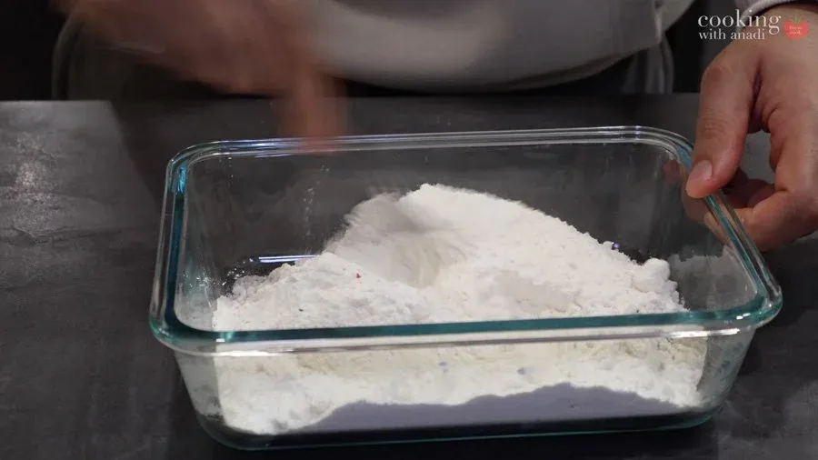 Flour mixture with salt, pepper, and baking powder in a glass baking dish for breading chicken.
