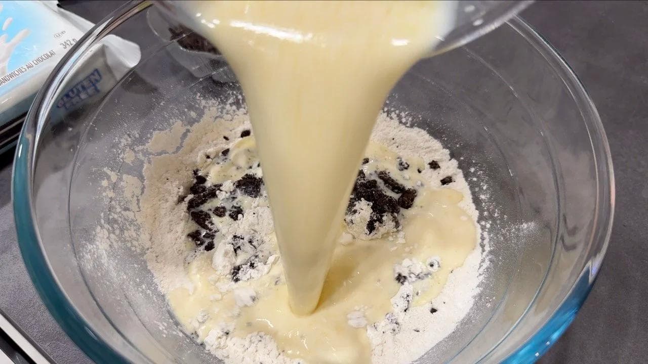 Wet batter with crushed Oreos being poured into a mixing bowl with dry ingredients and flour.