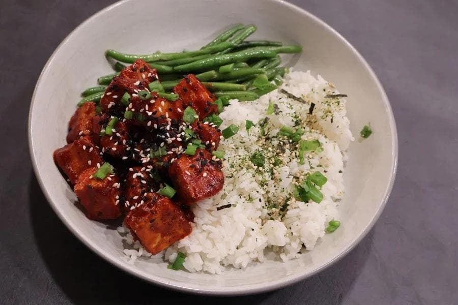 Crispy Korean-style air fryer tofu glazed with sesame seeds and green onions, served with white rice and steamed green beans.