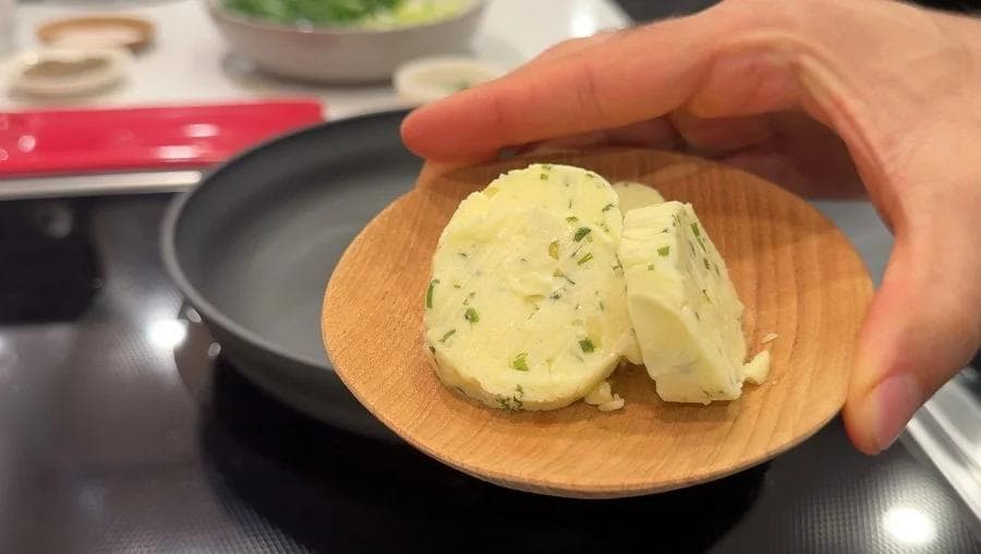 Garlic-chive butter sliced on a wooden plate, showing herb-flecked yellow butter ready for the filling.