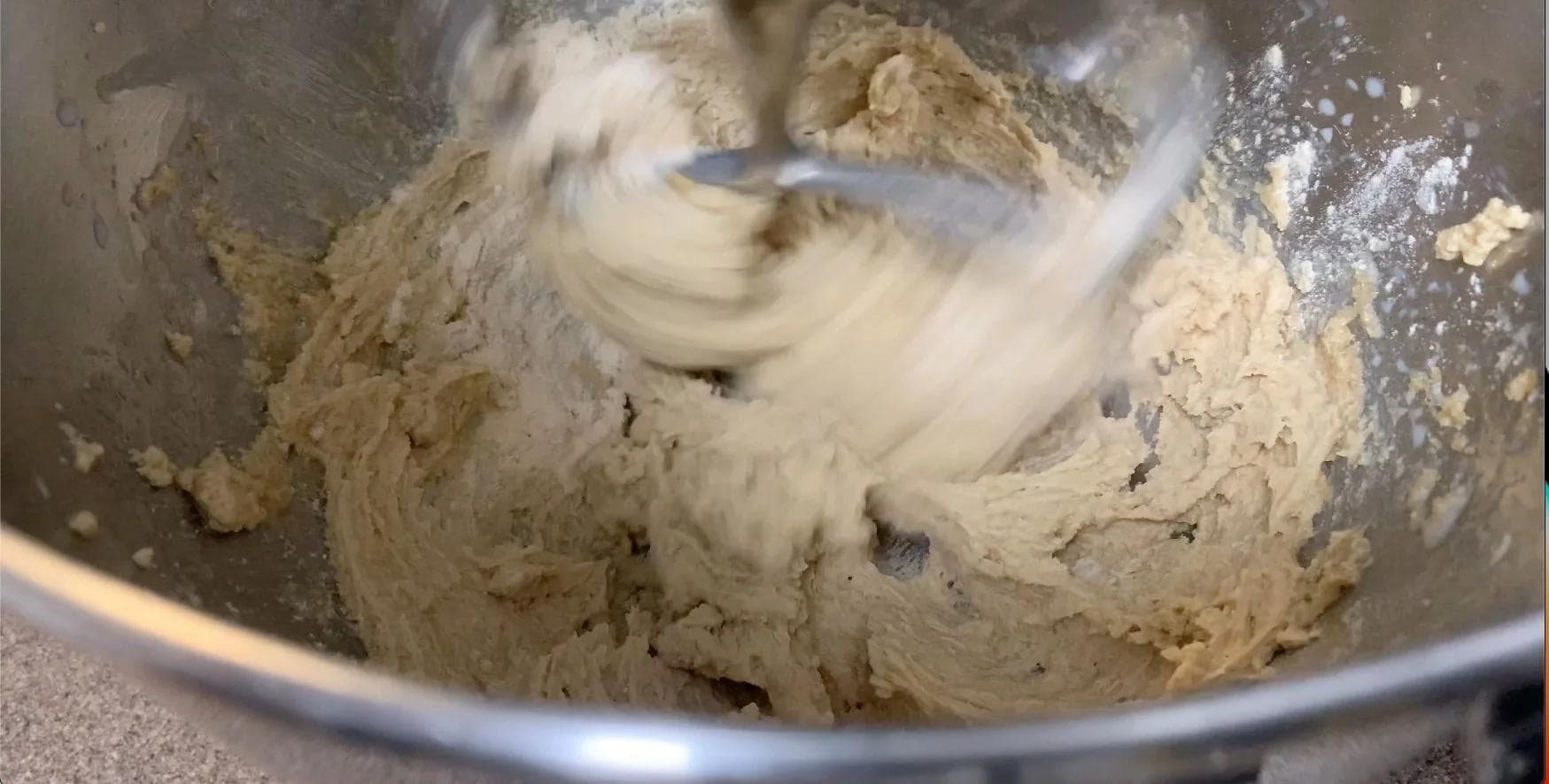 Cookie dough mixing in a stand mixer bowl, showing a smooth, creamy texture with flour incorporated.
