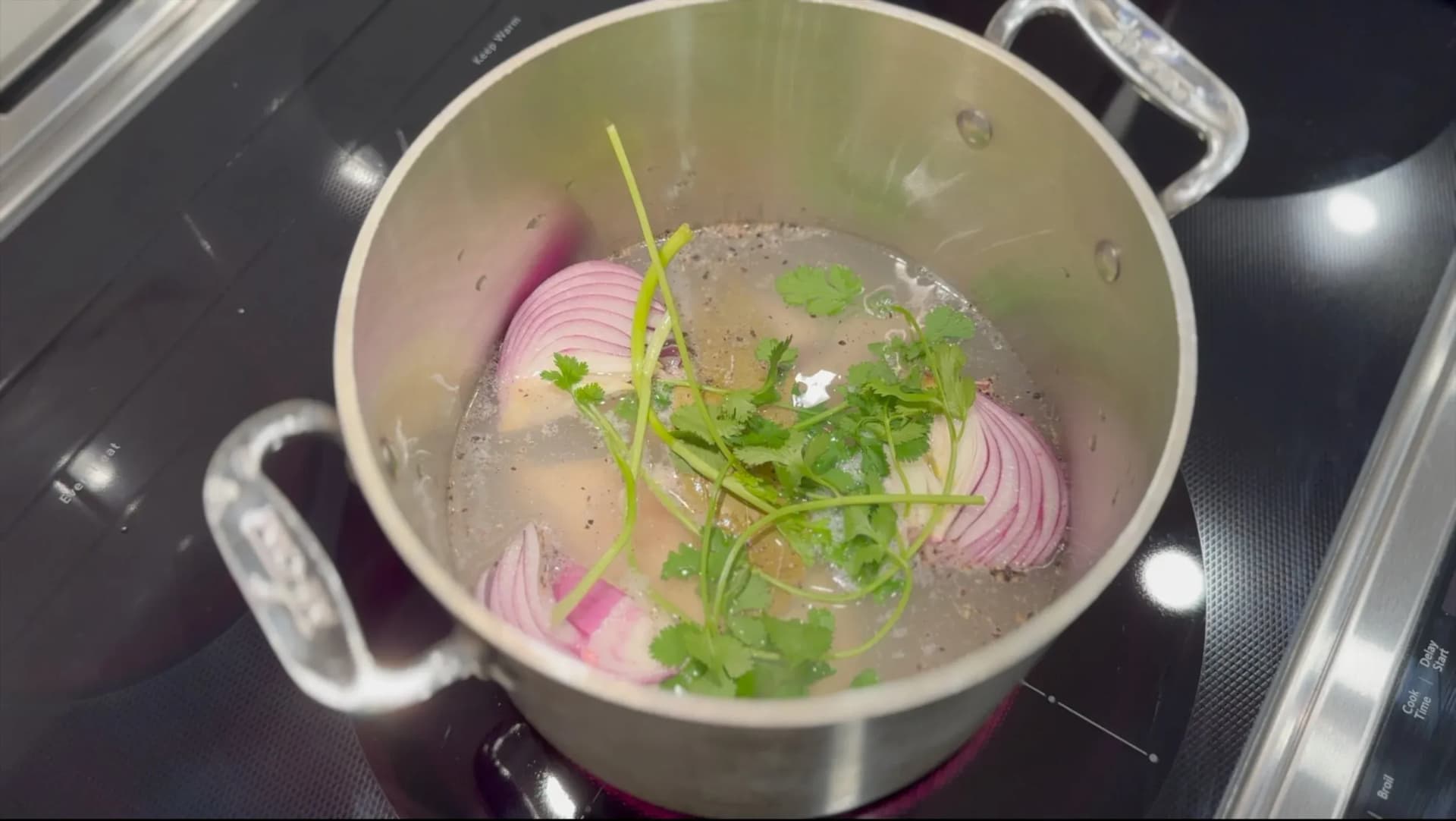 Pot of simmering chicken breast with sliced red onion and fresh cilantro in broth on stovetop.