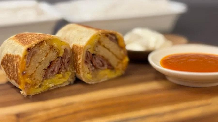 Sliced breakfast burritos filled with meat and hash browns, served with salsa sauce.