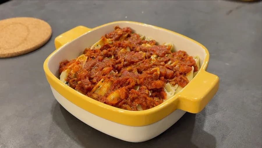 Cheesy stuffed shells with meat sauce in a yellow and white baking dish, ready to bake.