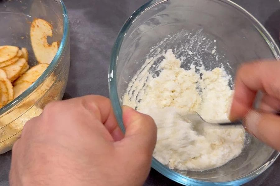 Hand mixing ricotta, maple syrup, and lime juice in a glass bowl with a spatula.