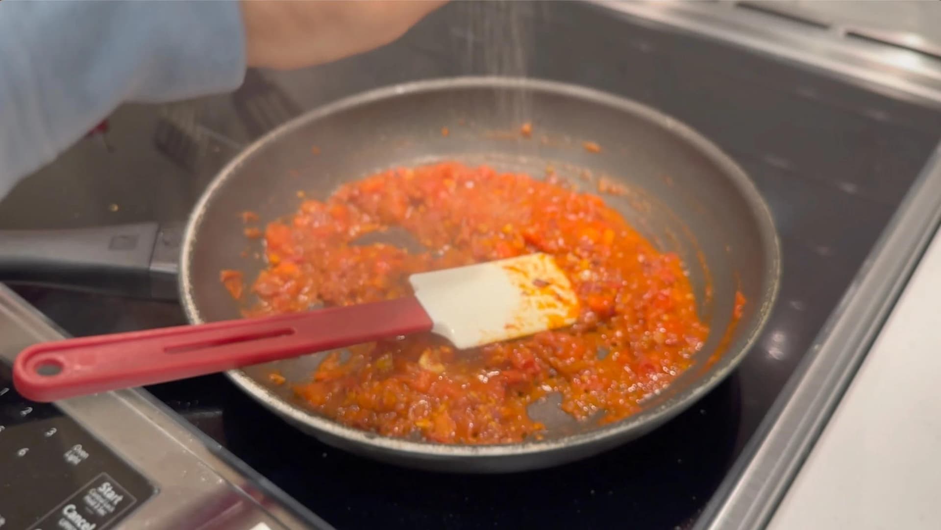 Red tomato mixture with spices cooking in a pan, being stirred with a spatula on stovetop.