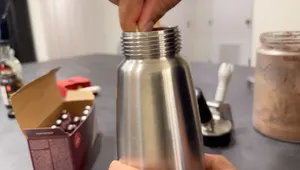 Hand screwing metal head onto whipped cream dispenser bottle.